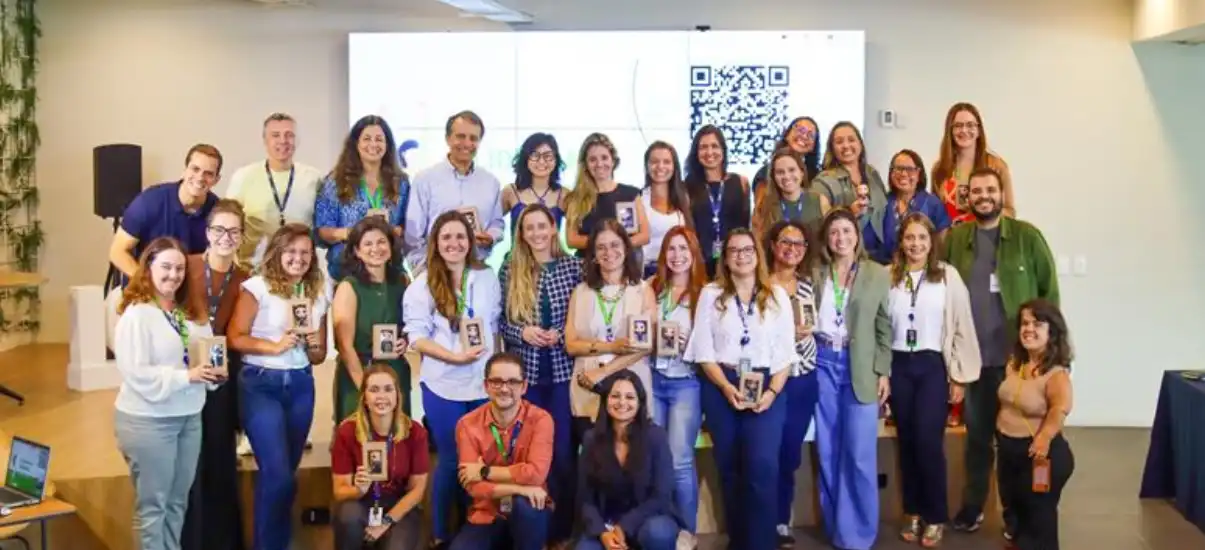 Grupo de profissionais participando de evento ou workshop com ambiente moderno, telas digitais e QR code ao fundo, promovendo networking e conhecimentos na área de tecnologia ou educação.