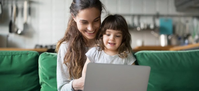 Mãe e filha sorrindo enquanto usam laptop em ambiente doméstico, representando conexão familiar, tecnologia e momentos felizes juntos.