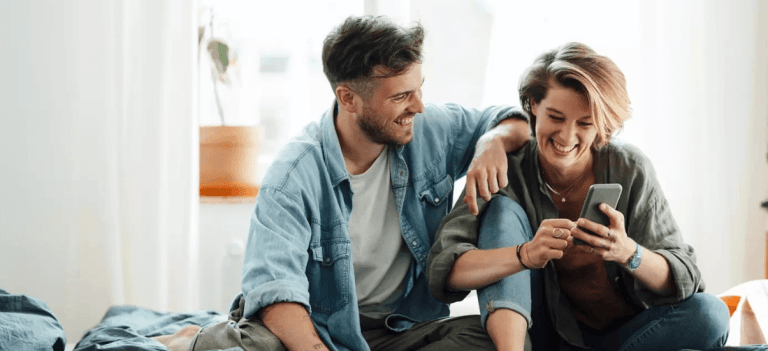 casal juntos sentados vendo o celular sorridentes