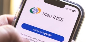 Celular na mão exibindo a tela de acesso ao Meu INSS com o botão “Entrar com gov.br”, ícone do serviço e indicador de sinal no canto superior direito.