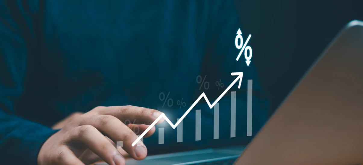 Mão apontando para gráfico de crescimento com setas e símbolos de porcentagem em fundo de escritório, sugerindo aumento de resultados e promoções